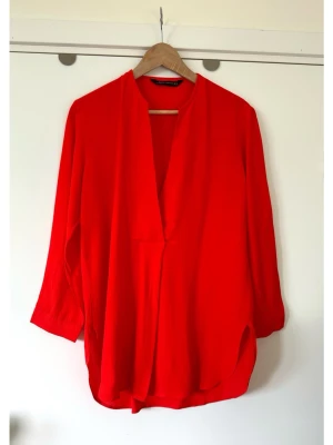 ZARA - Röd blus med v-ringning - storlek S / M - Härlig elektriskt röd blus från ZARA med långa ärmar och en V-ringning. Vid och luftig modell i storlek S, men passar även M om man vill ha det mer figurnära. Elegant vikning fram och rundad nederkant. Ärmsluten är försedda med en knapp. Viskos-blandning, så bra material som andas. Mycket gott skick, som ny!