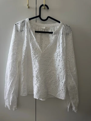 Vit broderad blus från H&M - Säljer en vit blus med broderade hålmönster Perfekt för en fräsch och somrig look. Tillverkad i bomull för en luftig känsla.