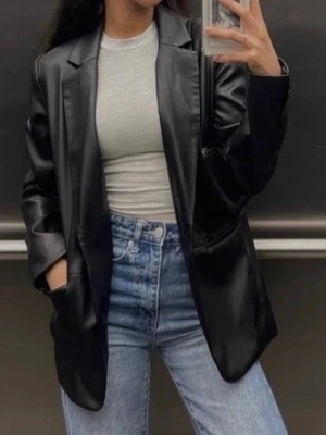 Svart oversized kavaj i fuskläder - Snygg svart oversized kavaj i fuskläder med klassisk krage och två knappar framtill. Kavajen har raka axlar, långa ärmar och flera fickor. Perfekt för en trendig och edgy look till jeans eller klänning.