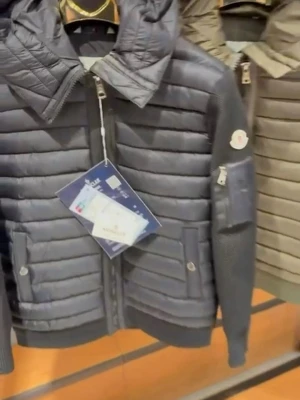 Svart pufferjacka från Moncler - Snygg svart pufferjacka från Moncler med quiltad design och stickade ärmar. Jackan har dragkedja framtill, fickor med knappstängning och en Moncler-logga på ärmen. Perfekt för kalla dagar med sin varma och stilrena look.
