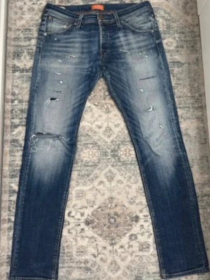 Blå jeans från Jack & Jones med slitningar - Säljer ett par blå jeans med slitningar från Jack & Jones. Byxorna har inga defekter och är väldigt stiliga. W33 L32