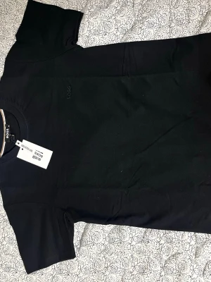 Svart t-shirt  - Snygg svart t-shirt med diskret logga på bröstet. Klassisk passform och rund halsringning, perfekt till jeans eller shorts. Tillverkad i mjuk bomull för en skön känsla hela dagen.