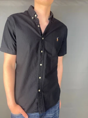 Kortärmad Ralph Lauren skjorta - Kortärmad Ralph Lauren skjorta Märke: Polo Ralph Lauren Storlek: L  Passform: Slimfit Färg: Svart Skick: Mycket bra Beskrivning: utan defekter. Modellen på bilden: 183 cm/ 75 kg