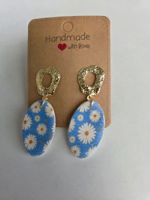 Blå handgjorda örhängen med prästkragar - Unika handgjorda örhängen med ovala hängen i blått med prästkragemönster. Överdel i guldtonad metall med organisk, ojämn form. Perfekta till midsommar! Örhängena är gjorda för hand av mig i polymerlera. 