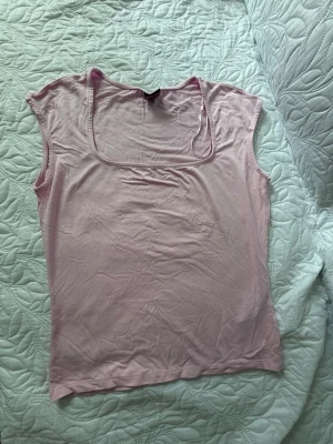 Ljusrosa topp från Gina Tricot - Söt ljusrosa topp från Gina Tricot med fyrkantig ringning och ärmlös design. Tillverkad i mjuk bomullsmix som känns skön mot huden. Perfekt att styla med jeans eller kjol för en fräsch look.