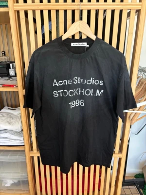 Svart Acne Studios t-shirt - Cool svart t-shirt från Acne Studios med tryck 'Acne Studios STOCKHOLM 1996' på bröstet. Klassisk rund hals och korta ärmar. Perfekt för dig som gillar stilrena plagg med en twist. Storlek M och i oanvänt skick.