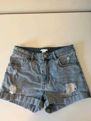 Blå denimshorts med slitningar - Snygga blå denimshorts med uppvikta benslut och slitna detaljer framtill och på bakfickorna. Klassisk femficksmodell med knapp och dragkedja. Perfekta för varma dagar och ger en avslappnad look.