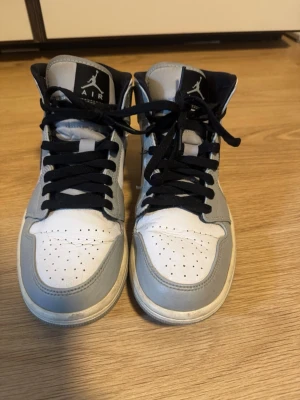 Nike Air Jordan 1 Mid grå/vit - Säljer ett par Nike Air Jordan 1 Mid sneakers i grått och vitt med svarta detaljer. Ovandelen är i läder.