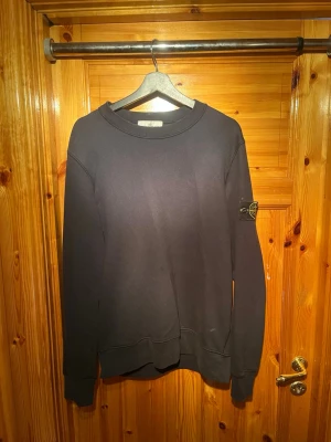 Svart sweatshirt från Stone Island - Säljer en svart sweatshirt från Stone Island med klassisk rund hals och ribbade muddar. Tröjan har den ikoniska Stone Island-loggan på vänster ärm och är tillverkad i mjukt bomullsmaterial. Perfekt för en avslappnad och stilren look. Köpare står för frakt  📦 