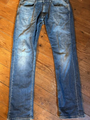 Blå raka jeans från Replay - Snygga blå jeans från Replay med klassisk femficksdesign och raka ben. Jeansen har en lätt tvättad look med slitningar framtill och bakfickor med diskreta sömmar. Perfekta för en avslappnad stil. Materialet är bomullsdenim.