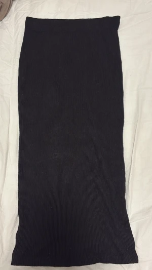 Svart ribbad långkjol - En svart långkjol med ribbad struktur. Kjolen har en rak passform och är enkel att matcha till olika stilar. Perfekt för dig som gillar minimalistiska plagg med en liten twist.