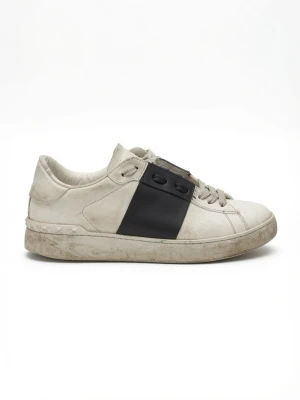 Valentino Garavani - Snygga vita sneakers från Valentino med en bred svart läderdetalj över sidan och nitar på hälen. Skorna har klassisk låg profil, vita snören och en chunky sula. Perfekta för dig som gillar stilrena men ändå unika sneakers.
