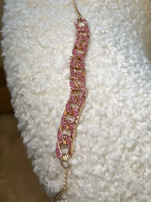 Guldhalsband  med rosa stenar - Snyggt halsband  i guldfärgad metall med chunky kedjelänkar täckta av glittrande rosa stenar. Perfekt statement-piece för dig som gillar att sticka ut och addera färg till din stil. Länkarna har en cool, modern design och halsbandet  har ett tunt kedjelås.