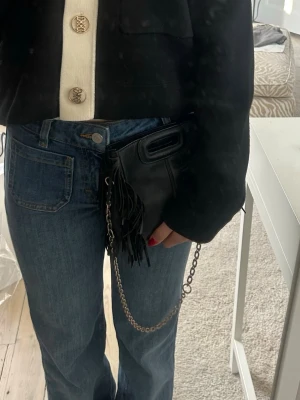 Maje väska mini - Säljer en svart majeväska i skinn med silverkedja. Man kan ha den som en shoulderbag men jag gillar även att använda den som en clutch och bara hålla i den. Den är i storlek mini med måtten 17x14x6cm. Jag köpte den för några år sedan för ca 3000kr. Färgen på kedjan har börjat gå bort lite men går att byta ut till en ny kedja. Den lilla Maje texten håller också på att gå bort men annars är väskan i bra skick! Därför säljer jag den för 1000kr. 
