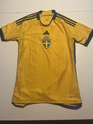 Sverige fotbollströja Adidas gul S - Äkta Sverigetröja från Adidas affären Klassiska Adidas-ränder på axlarna och tillverkad i lätt, ventilerande material. Pris går att diskuteras vid snabb affär