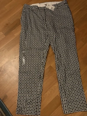 Nya Svarta och vita mönstrade byxor/slacks från H&M - Snygga byxor/slacka  med svartvitt grafiskt mönster och rak passform. Byxorna har hög midja och är tillverkade i ett lätt tyg som känns bekvämt. Perfekta för dig som vill sticka ut med ett coolt print.