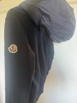 Zip hoodie från Moncler - Ziphoodie från Moncler med klassisk Moncler-logga på ärmen och stor huva i kontrasterande material. Hoodien har en stilren look och passar perfekt för dig som gillar exklusiva och unika plagg