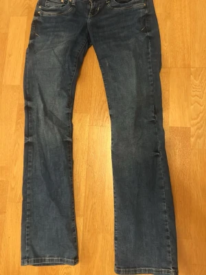 Blå bootcut jeans från ltb  med slitningar - Säljer ett par klassiska blå bootcut ltb jeans med lätt slitna detaljer och fem fickor. Jeansen har normal midja och är tillverkade i denim med en snygg tvätt. Perfekta för en avslappnad och trendig look.