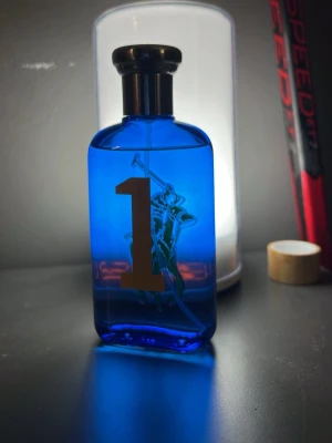 Ralph Lauren Polo Blue parfym - Snygg parfymflaska från Ralph Lauren Polo Blue med en djupblå färg och en stor siffra 1 på framsidan. Flaskan har en klassisk form och är dekorerad med den ikoniska polospelaren. Perfekt för dig som gillar stilrena och sportiga dofter.