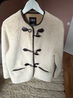 Beige pälsjacka från Zara - Säljer denna  beiga jacka ifrån Zara med fina knapp detaljer och passar perfekt nu till våren just för att de inte är för varm eller kall.