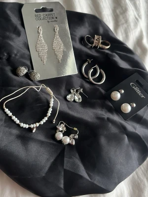 (SILVER) Mix av örhängen från Glitter & Red Carpet - Säljer ett set med flera olika örhängen, bland annat glittrande droppformade från Red Carpet Collection och klassiska pärlörhängen från Glitter. Flera örhängen i silverfärg, vissa med pärlor och stenar. Perfekt för dig som vill variera din stil. (Priset är lika mycket som bara en av dem här skulle kosta)