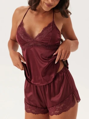 DORINA Pyjam Pyjamasset Lyra-satin - Slutsålt vinrött pyamasset från Dorina i satin med spetsdetaljer. Setet består av ett linne med tunna, korsade axelband och v-ringning samt matchande shorts med spetskant. Materialet är glansigt och mjukt, perfekt för en lyxig känsla.
