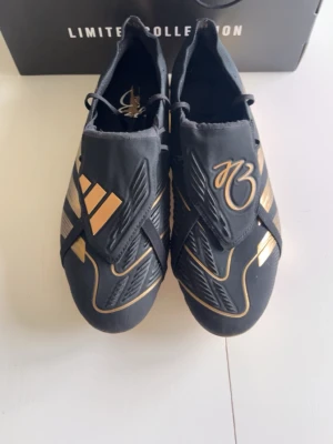 Adidas Predator elite FG  - Säljer ett par svarta Adidas Predator fotbollsskor i Limited Edition med guldiga detaljer och logga. Skorna har en modern design med snörningsfritt system och guldmetallic sula. Tillverkade i syntetmaterial för bästa grepp och känsla på planen.