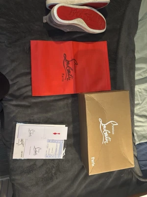 Gråa Louboutin sneakers i mocka - Snygga gråa sneakers från Christian Louboutin i mjuk mocka med klassisk röd sula och vita kanter. Skorna har lågt skaft, rund tå och matchande grå skosnören. Kommer med originalkartong, dustbag och certifikat.