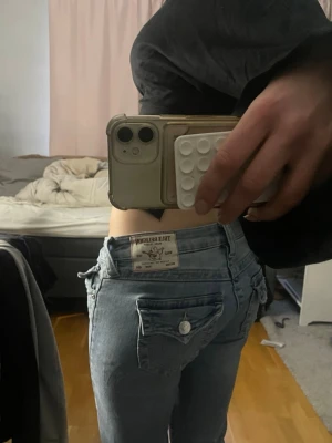 Ljusblå bootcut jeans True Religion - Säljer ett par ljusblå bootcut jeans från True Religion med knappar på fickorna. Jeansen är normala o storlek och skön passform. Defekter är att de har slitningar nertill.