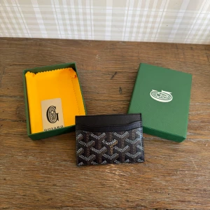 Svart kortfodral från Goyar* - Säljer ett elegant svart kortfodral från Goyar* med deras ikoniska mönster. Perfekt för att hålla dina kort organiserade och stiliga. Kommer i originalförpackning med en gul putsduk.