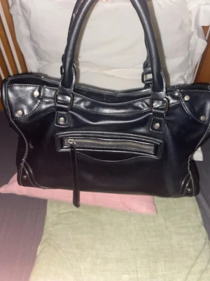 Svart balenciaga-inspirerad väska - Jag säljer en svart väska från Gina Tricot (jag betalade 500kr för den). väskan är inspirerad av Balenciagas city bag. den har silver detaljer och är inte av djurmaterial! jättesnygg och passar framförallt om du gillar ”stockholmstil”💕🫶🏼 jag har tagit väl hand om den så det är i princip inga tecken på användning💕💕 skriv för mått på väskan!!