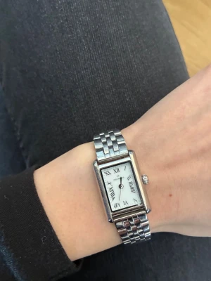 Silverfärgad rektangulär klocka Hockberg - Stilren klocka från mockberg med rektangulärt vitt ur och romerska siffror. Armbandet är i silverfärgad metall med klassisk länkdesign. Perfekt accessoar för dig som gillar tidlös och elegant stil.