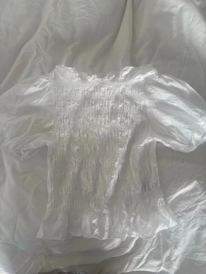 Vit smockad blus från HM - Supersöt vit blus från Zara med smockad överdel och puffiga korta ärmar. Tillverkad i ett lätt och luftigt tyg som ger en romantisk vibe. Perfekt att styla med jeans eller kjol för en trendig look.