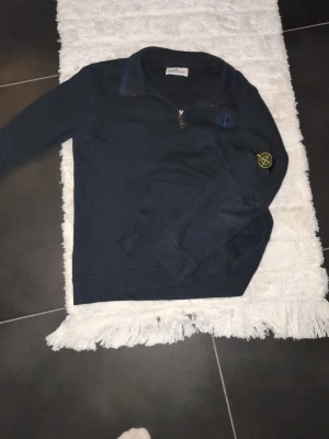Mörkblå ziptröja från Stone Island - Snygg mörkblå långärmad ziptröja från Stone Island med klassisk patch på ärmen och halv dragkedja framtill. Tröjan har en stilren design med krage och är perfekt för dig som gillar streetwear och exklusiva detaljer.