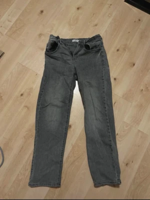 Grå raka jeans (Vilgot) - Ett par grå jeans med rak passform. Klassisk femficksmodell med dragkedja och knapp framtill. Jeansen har en avslappnad look och är tillverkade i denim. Perfekta för en chill och stilren outfit.