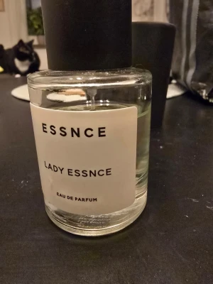 Lady Essnce Eau de Parfum - Minimalistisk parfymflaska från ESSNCE med svart lock och transparent glas. Doften heter Lady Essnce och är en Eau de Parfum. Flaskan har en enkel vit etikett med svart text och en stilren, modern design.
