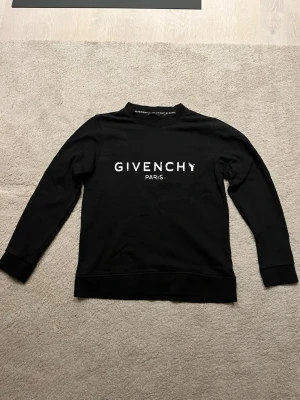 Svart Givenchy Paris sweatshirt - Snygg svart sweatshirt från Givenchy Paris med vit logga tryckt på bröstet. Tröjan har rund halsringning, långa ärmar och ribbade muddar vid ärmslut och nederkant. Perfekt för en stilren och trendig look. Tröjan är äkta och pris kan diskuteras! Med vänliga hälsningar milo
