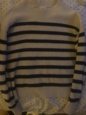 Randig stickad tröja i vitt och svart - Säljer en ribbstickad tröja med breda svarta och vita ränder. Tröjan har rund halsringning, långa ärmar och en avslappnad passform. Perfekt för lager-på-lager och enkel att styla till jeans eller kjol.