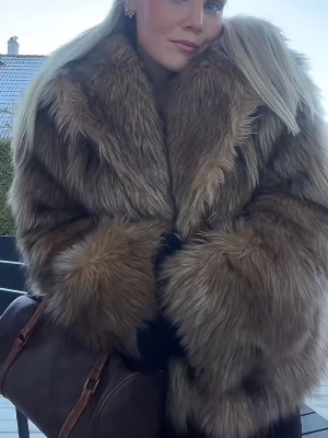 Brun fluffig pälsjacka - Säljer en brun, fluffig pälsjacka med breda ärmar och klassisk krage. Jackan har ett lyxigt och voluminöst utseende, perfekt för att hålla sig varm under kalla dagar. 