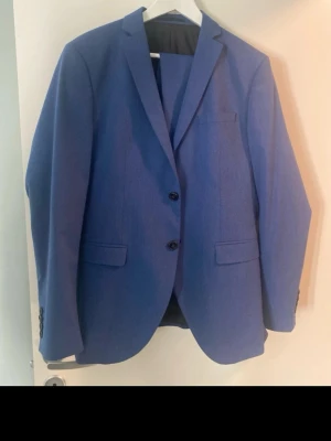 Blå kavaj från Carreman - Snygg blå kavaj från Carreman, designad i Frankrike. Klassisk modell med två knappar framtill, fickor med lock och slät finish. Perfekt för dig som vill ha en stilren och modern look. Passar 14-16 åringen 