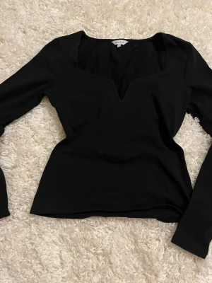 Svart långärmad topp från Bubbleroom - Snygg svart topp från Bubbleroom med lång ärm och djup v-ringning. Modellen är figurnära och har en stilren design som passar perfekt till jeans eller kjol. Tillverkad i mjukt material för en bekväm känsla.