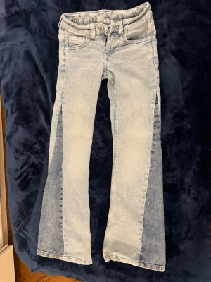 Unika low waist jeans from HM - Säljer ett par ljusblå jeans från H&Mmed cool utsvängd passform och kontrasterande mörkare paneler längs benen. Klassisk femficksmodell med dragkedja och knapp. Perfekta för dig som vill sticka ut med en unik denimlook. Jeansen är low waist och väldigt snygga på. Originalpris 349