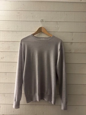  stickad tröja från A DAY’s MARCH - En stilren ljusgrå stickad tröja med rund halsringning och långa ärmar. Tröjan har ribbade muddar vid ärmslut och nederkant. Perfekt för lager på lager och enkel att matcha med olika outfits.