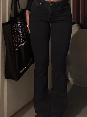 Svarta bootcut jeans  - Säljer ett par svarta bootcut jeans med mid midja och klassisk femficksdesign. Jeansen har en snygg passform som sitter tight upptill och släpper ut vid benen. Perfekta till en trendig vardagslook.