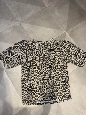 Leopardmönstrad t-shirt i beige och svart - Snygg t-shirt med leopardmönster i beige och svart. Klassisk rund halsringning och korta ärmar. Perfekt för dig som vill sticka ut med ett djurmönster. Materialet känns mjukt och bekvämt mot huden.