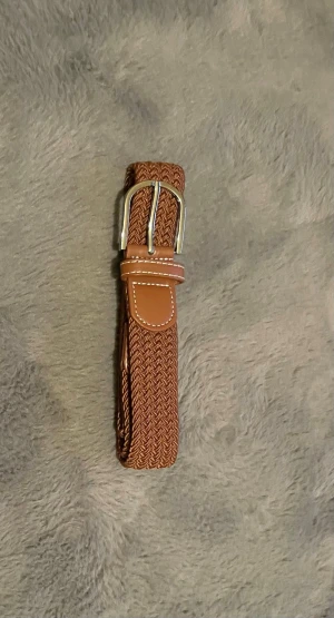 Brunt flätat bälte med silverfärgat spänne - Snyggt brunt flätat bälte med silverfärgat spänne och detaljer i skinnimitation. Perfekt accessoar för att lyfta din outfit med en klassisk touch. Passar till både jeans och chinos. Obs kan upphämta i södra Stockholm 