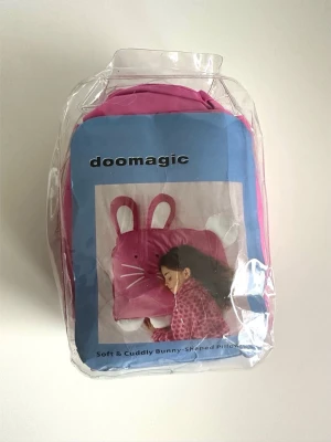 Doomagic rosa kaninformad kuddfodral - Supersöt Doomagic kaninformat örngott i rosa, med vadderade öron och svans. Tillverkad av 100% bomull med 250 trådtäthet. Passar standard/queen size kuddar. Maskintvättbar. Helt ny i förpackning. 