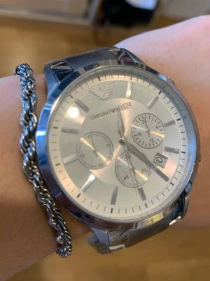 Emporio Armani silverfärgad klocka - Stilren klocka från Emporio Armani i silverfärgat stål med rund urtavla och tre mindre subdials. Klockan har datumvisning och klassisk länkarmband i metall. Perfekt accessoar för en modern look.