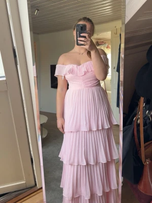 Ljusrosa offshoulder långklänning - Superfin ljusrosa långklänning med offshoulder och volangdetaljer. Klänningen har plisserad kjol i flera lager och. Storlek M och med prislapp kvar. Säljer då jag har en annan och returkostnaden var väldigt hög. Jag är 1.67-68 lång. Pris kan diskuteras!