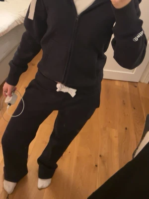 Svarta mjukisbyxor från russemerch  - Svarta mjukisbyxor från russemerch med vit dragsko i midjan. Byxorna har en avslappnad passform och är perfekta för chill dagar. Klassisk design med diskret logga på benet och mjukt material som känns skönt mot huden.